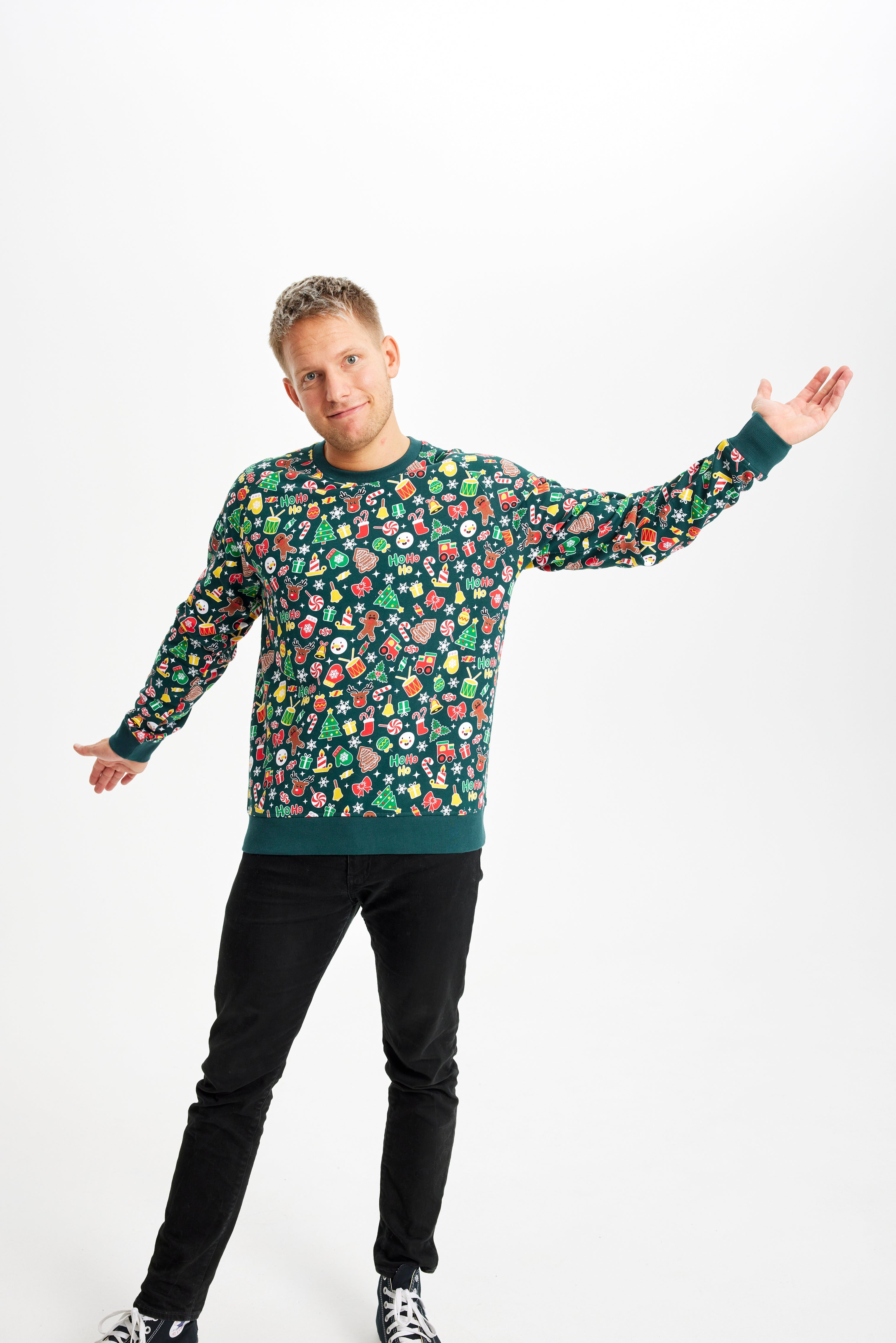 En mand med armene til siden iført en grøn julesweater med julemønster.